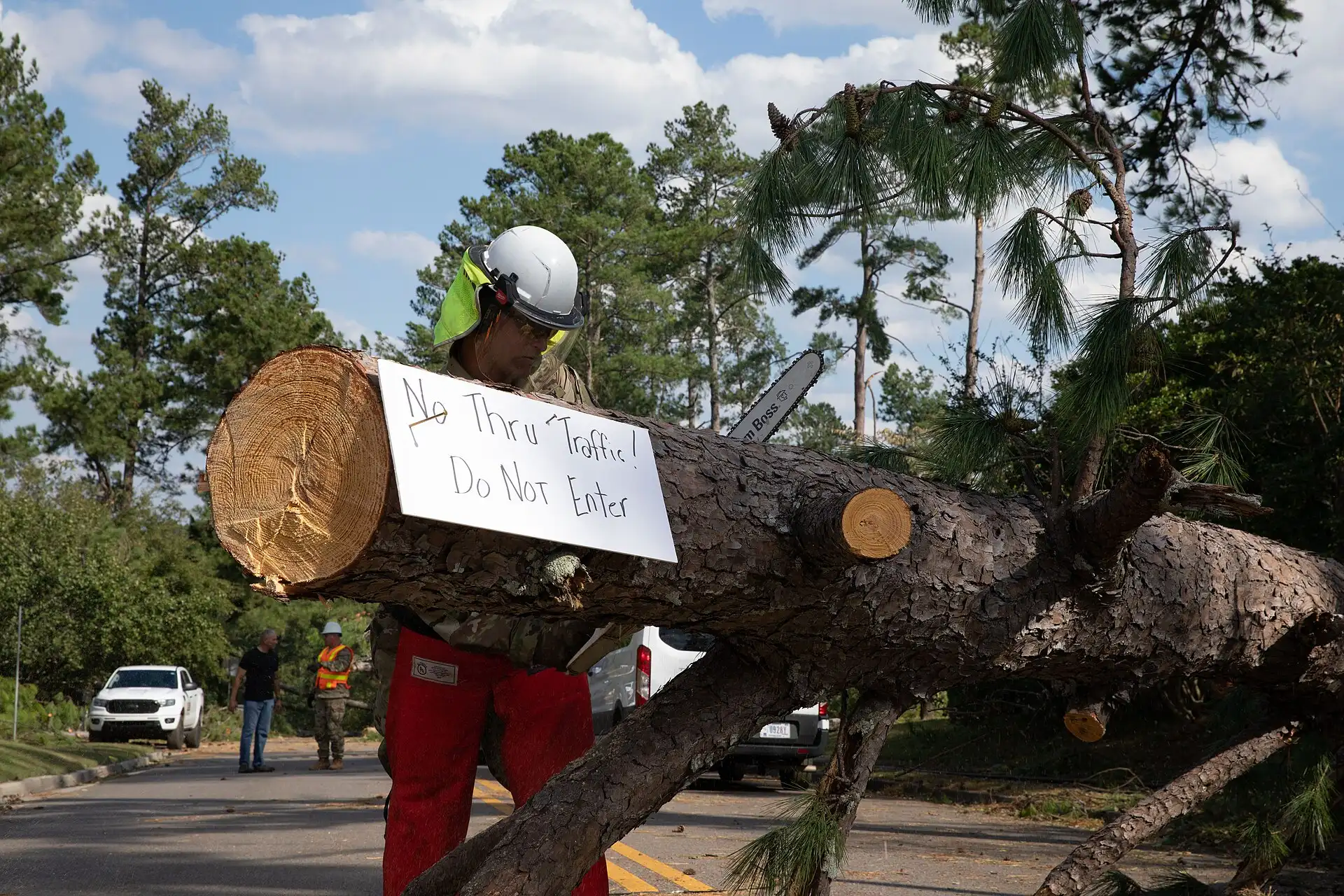 Crew member in hard hat carrying a cut log section during storm cleanup